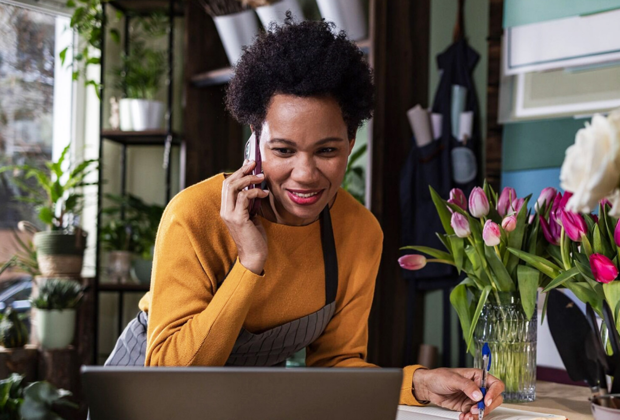 a woman talking on a phone while writing in front of a laptop
